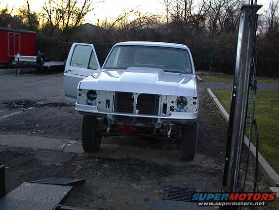 White Ford Bronco with hood scoop, open driver door, and missing grille, parked outdoors