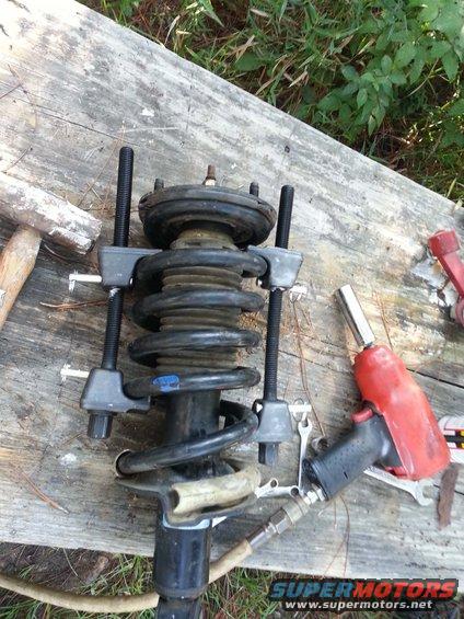 Car strut assembly with spring compressor tool attached, air impact wrench nearby