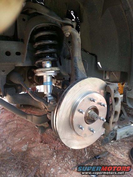 close-up of a vehicle's front suspension with a new shock absorber and brake rotor