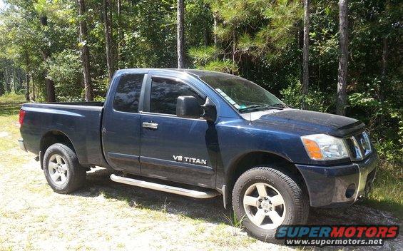 2006 Nissan Titan pickup truck, dark blue, parked on dirt with trees in background