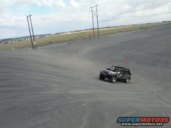 Gray 2005 Jeep Wrangler driving on a sand dune with a red flag on the antenna