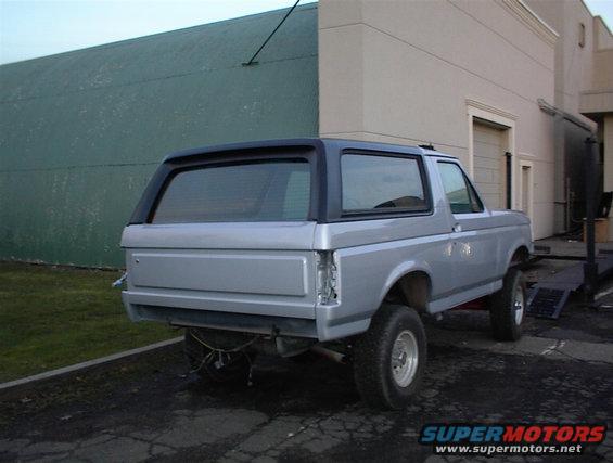 1990 Ford Bronco, rear view, silver paint, black top, parked outside building