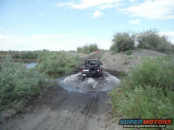 Black 2005 Jeep Wrangler driving through water on a dirt path