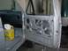 1990 Ford Bronco - The interior of a silver vehicle is shown with the driver's door open, revealing the removed door panel and a box of rags on the floor.