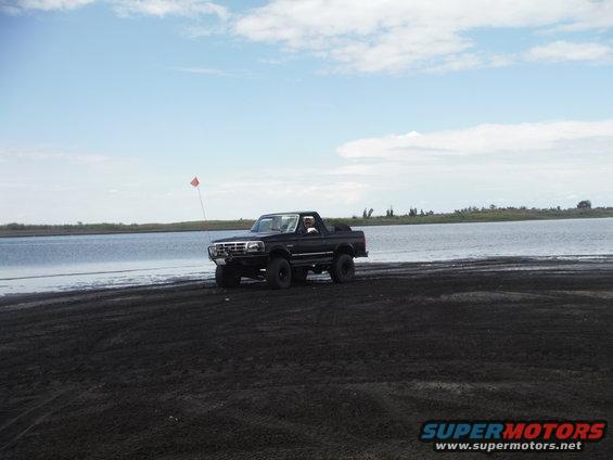 Black Ford Bronco driving on a sandy beach next to a body of water