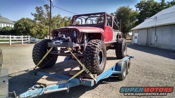 Red 1985 Jeep CJ7 on a trailer with large off-road tires and a roll cage