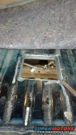 cutout in vehicle floor showing fuel lines and a wooden support, with a marker pen nearby