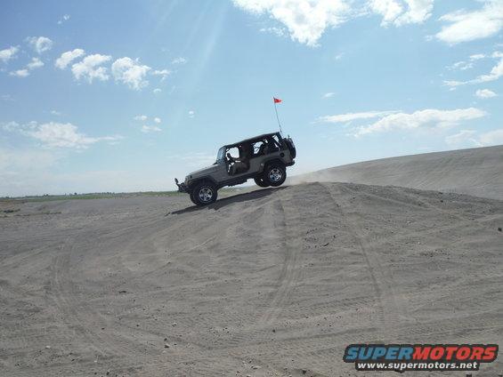 Jeep Wrangler driving up a sand dune with a red flag on top