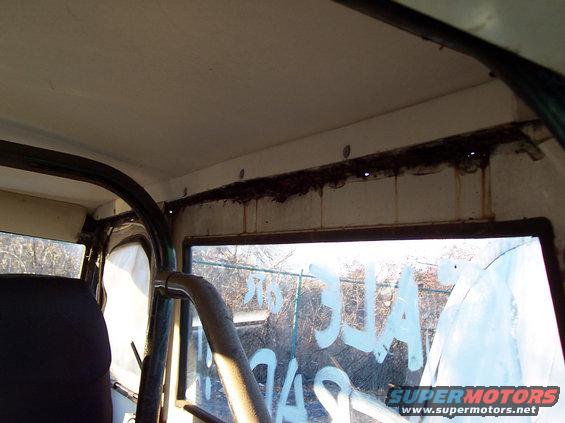 Interior view of a vehicle showing a roll cage, dark seat, and writing on the window