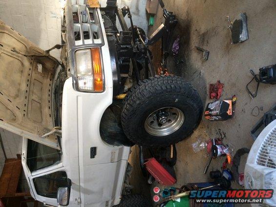 White Ford Bronco with hood open, showing front end and tire. Appears to be in a garage