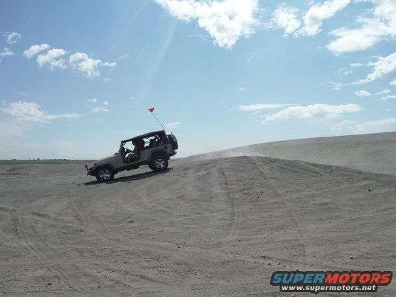 Silver Jeep Wrangler driving up a sand dune, red flag on antenna