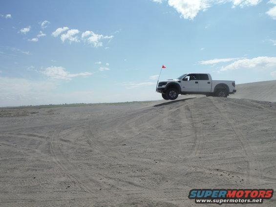 White pickup truck airborne over a sand dune with a red flag on an antenna