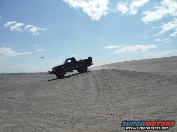 Black pickup truck on sand dune with flag