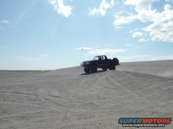 Black pickup truck with an orange flag on a sand dune under a blue sky