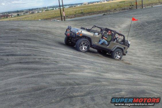 Jeep Wrangler driving up a sand dune with a red flag on the back
