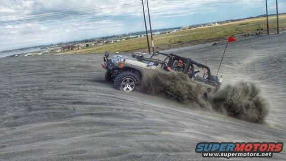 Tan Jeep Wrangler driving on a sand dune, kicking up dust