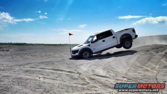 White pickup truck airborne on a sand dune with a red flag nearby