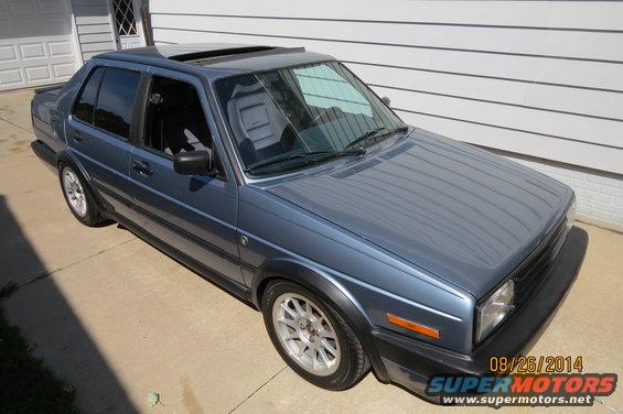 1990 Volkswagen Jetta sedan, blue, with sunroof and aftermarket wheels, parked in front of a garage