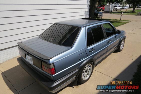 Blue 1990 Volkswagen Jetta sedan with a rear spoiler and aftermarket wheels, parked on a driveway
