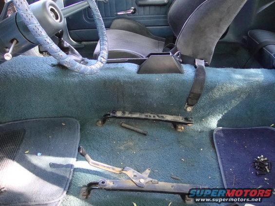 Car interior with blue carpet and seats, showing removed seat rails and steering wheel