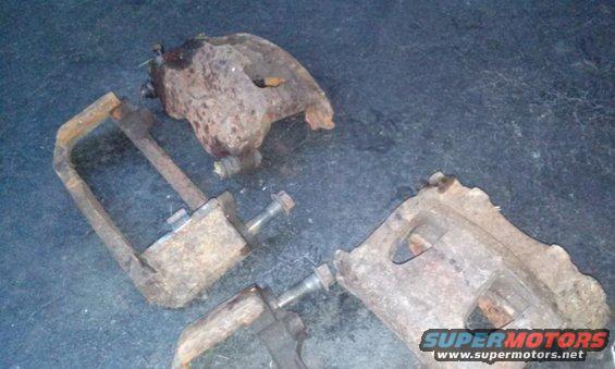 Rusty brake calipers and a C-clamp tool on a dark surface