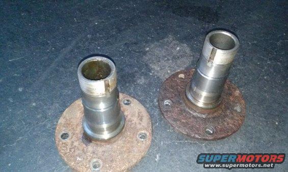 Two rusty wheel hubs with splined shafts sit on a dark surface
