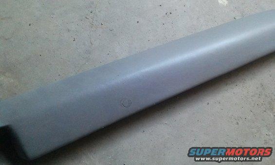 Gray plastic trim piece with a circular indentation, lying on a concrete surface