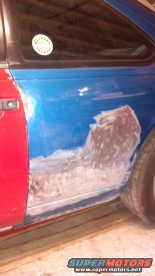 car door with red and blue paint, body filler applied to the blue section, and a circular sticker on the window