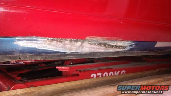 Red car body panel with blue section showing body filler and rust repair, resting on red car lift