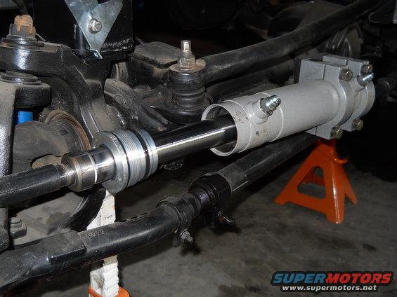 Close-up of a power steering cylinder being installed on a vehicle's steering linkage, supported by jack stands