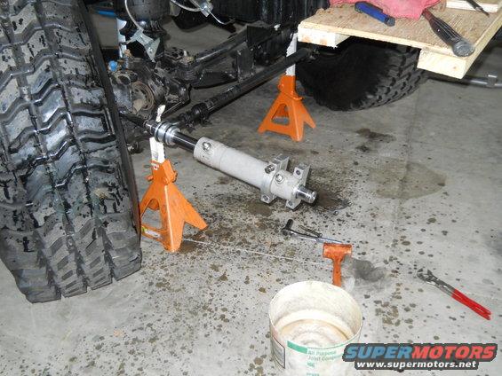 Vehicle's front wheel and suspension components on jack stands, with a steering stabilizer cylinder removed