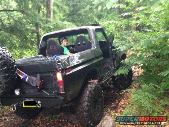 Modified 1978 Ford Bronco with racing seats and large tires off-road in woods