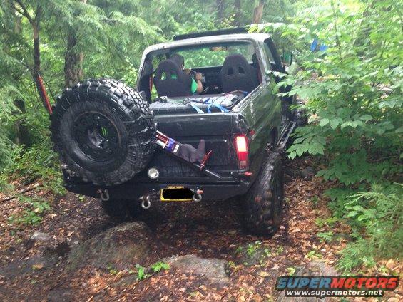 Black SUV with large spare tire on back, driving on a rocky, wooded trail