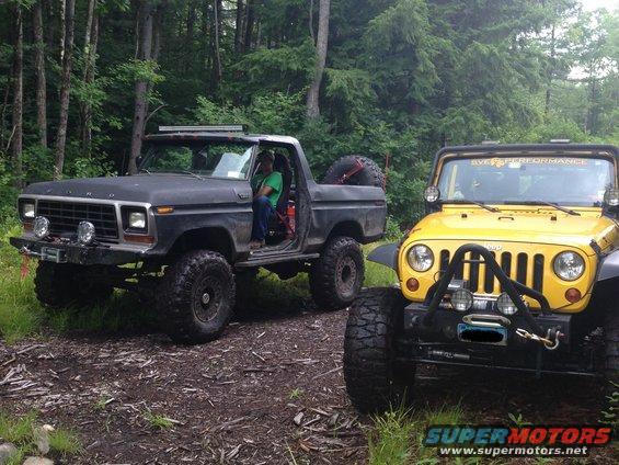 1979 Ford Bronco and a yellow Jeep parked on a dirt path in a wooded area