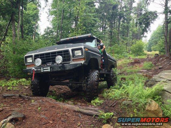 Black 1979 Ford Bronco with lifted suspension and off-road tires navigating a wooded trail
