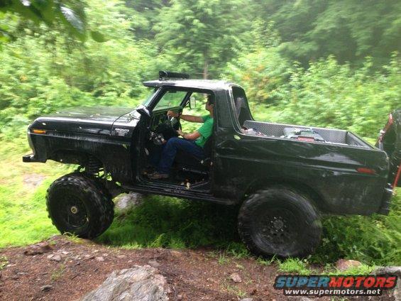 Black 1978 Ford Bronco off-roading on a dirt path with large tires and lifted suspension