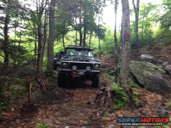 Black Ford Bronco with winch on front bumper driving on a dirt trail through woods