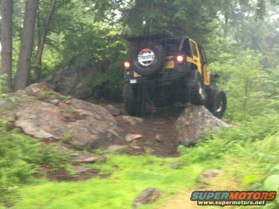 Yellow Jeep Wrangler climbing over rocks on a trail