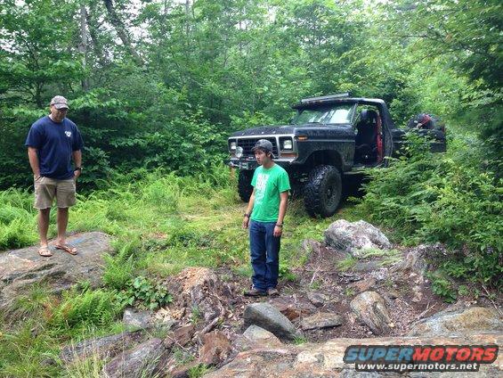 Black Ford Bronco with lifted suspension and off-road tires parked on a rocky trail with two men standing nearby