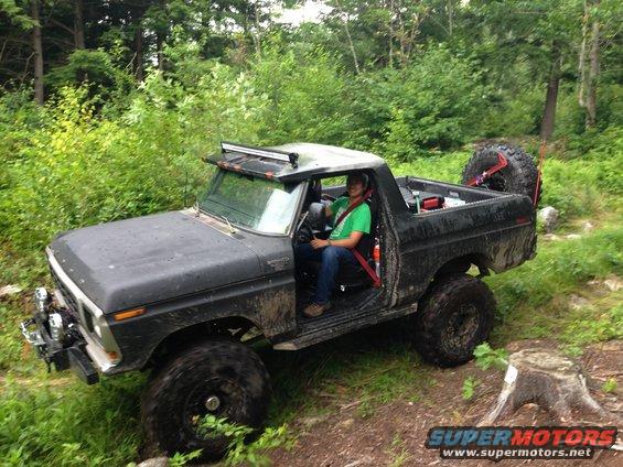 Modified black Ford Bronco with large tires and a light bar, driven off-road
