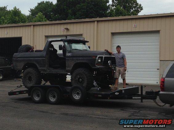 Guy next to a lifted black Ford Bronco on a trailer, doors removed, with a spare tire in the bed