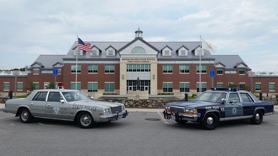 Two police sedans, one silver and one blue, parked outside the Rhode Island State Police Public Safety Complex