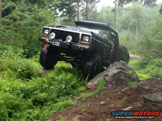 Black 1979 Ford Bronco on rocks, front-left tire lifted, winch visible