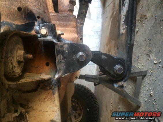 Close-up of a black suspension bracket attached to a rusty vehicle frame, with a tire visible