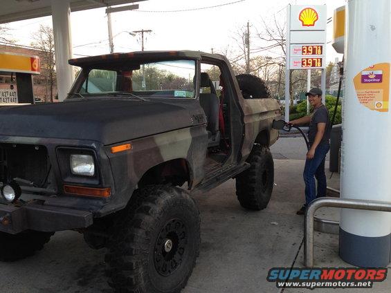 1979 Ford Bronco with camouflage paint and large tires fueling up at a Shell station