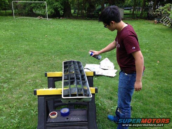 Black and chrome car grille on sawhorses, being spray painted by a person