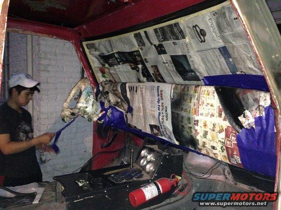 Red vehicle interior with newspaper protecting surfaces, a person is peeling tape, and a fire extinguisher is visible