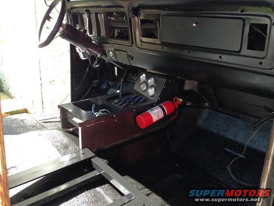 Interior of a 1978 Ford Bronco with black flooring, a wooden center console, and a fire extinguisher mounted on the passenger side