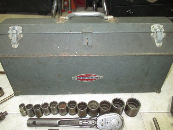 Gray metal toolbox with a row of socket wrenches and a ratchet in front. The toolbox has a red and silver Craftsman logo