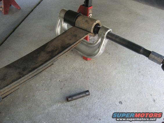 Leaf spring being compressed by a C-clamp, with a jack stand in the background